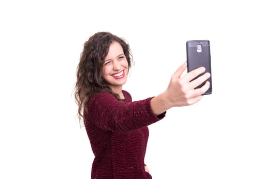 Happy young woman taking self portrait photography through smart phone over white background.