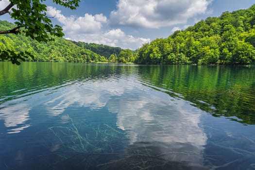 Beautiful turquoise water with puffy clouds reflected in a lake. Green lush forest, Plitvice Lakes National Park UNESCO World Heritage in Croatia