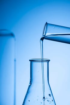 Filling an Erlenmeyer flask from a test tube against a blue-toned studio background.