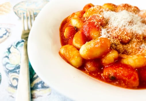 Portion of gnocchi in tomato sauce with grated parmesan cheese served in a white ceramic plate. Italian food and cuisine.