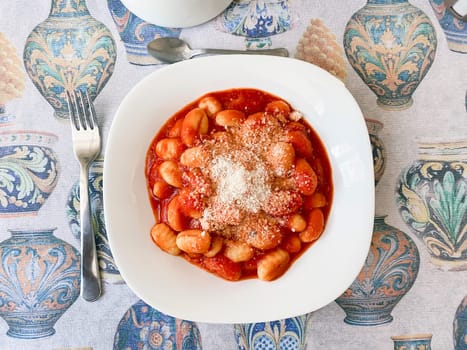 Top view of a portion of gnocchi in tomato sauce with grated parmesan cheese served in a white ceramic plate. Italian food and cuisine.