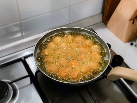 frying round meatballs in a pan with boiling oil. Homemade food. Modern domestic kitchen
