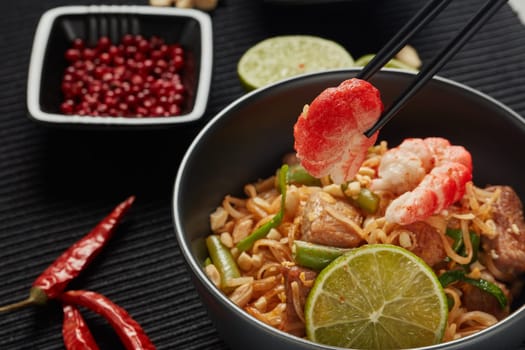 Pad Thai. Stir-fried rice noodles with chicken meat, shrimps,  scrambled egg, peanuts, vegetables and sauce in bowl. Thai food. Setting table.