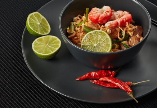 Pad Thai. Stir-fried rice noodles with chicken meat, shrimps,  scrambled egg, peanuts, vegetables and sauce in bowl. Thai food. Setting table.