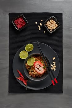 Pad Thai. Stir-fried rice noodles with chicken meat, shrimps,  scrambled egg, peanuts, vegetables and sauce in bowl on gray slate background. Top view. Thai food. Setting table
