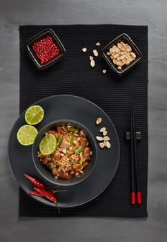 Pad Thai. Stir-fried rice noodles with chicken meat,  scrambled egg, peanuts, vegetables and sauce in bowl on gray slate background. Top view. Thai food. Setting table