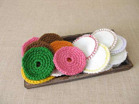 Crocheted and sewn, reusable and washable cosmetic pads made of colorful wool or cotton fabric on a tray