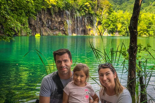 Portrait of happy family with lake and waterfalls in background, on vacations in stunning Plitvice Lakes National Park, a UNESCO World Heritage site