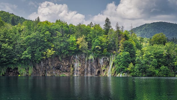 Beautiful waterfall illuminated by sunlight with reflections in lake. Green lush forest, Plitvice Lakes National Park UNESCO World Heritage in Croatia