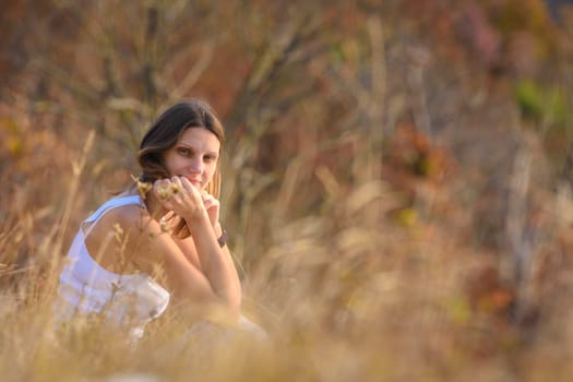 A girl sits in a field, against a background of blurred wildflowers and looks into the frame