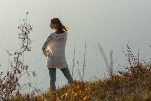 A girl stands on a hill by the sea and looks around, rear view