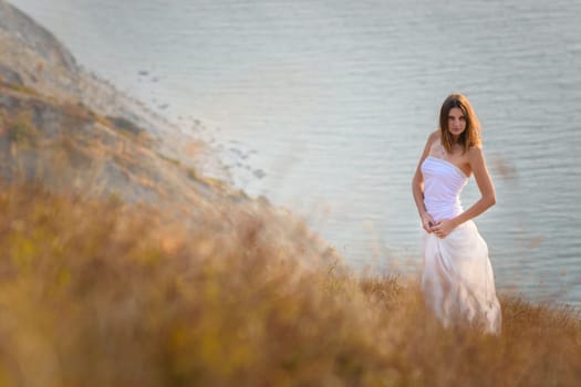 A beautiful slender girl stands on a hillock against the background of the sea