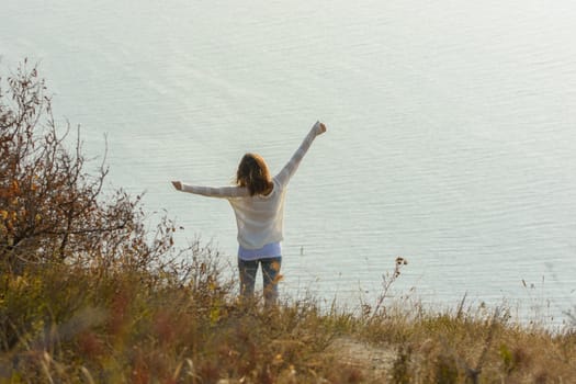 Happy girl happily raised her hands up enjoying the seascape, view from the back
