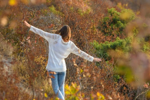 Slender beautiful girl walks through the forest making her hands an airplane, a view from the back