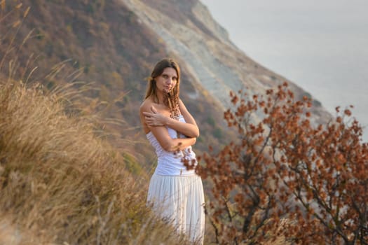A girl embraces wildflowers on the background of a beautiful mountain and sea landscape