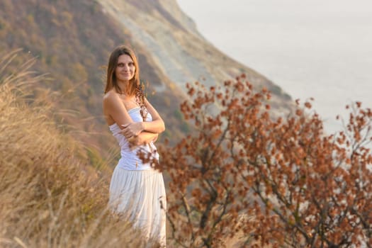 A beautiful girl stands on a rocky seashore and hugs wildflowers