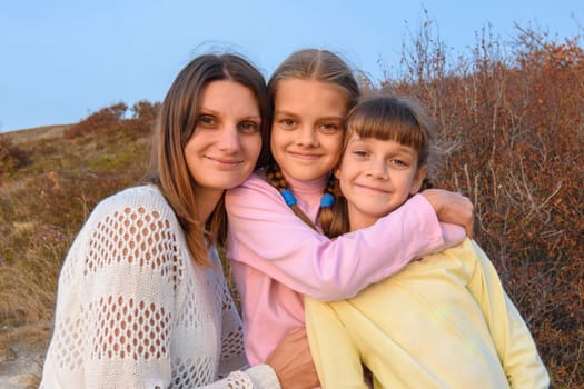Portrait of a happy girl with two daughters on the background of nature