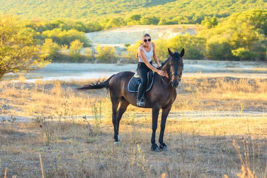 Girl with glasses strokes a horse riding in the autumn forest