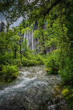 Rushing river and natural window in tree branches with a view on tall waterfall. Plitvice Lakes National Park UNESCO World Heritage in Croatia