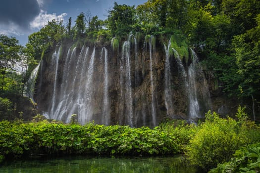 Streaks of water from waterfall illuminated by sunlight. Little pond in green lush forest. Plitvice Lakes National Park UNESCO World Heritage, Croatia