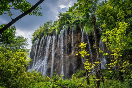 Streaks of water on tall waterfall illuminated by sunlight naturally framed by branches. Plitvice Lakes National Park UNESCO World Heritage in Croatia