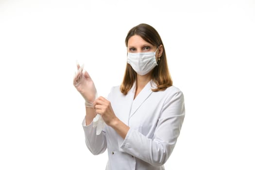 Girl doctor puts on transparent medical gloves on her hands and looks into the frame