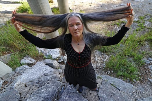 An older woman dreamily stretches her very long hair upwards