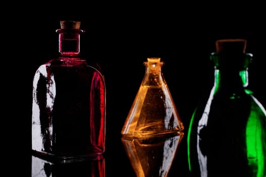 Still life of three colored decorative bottles with corks on glass against black background.