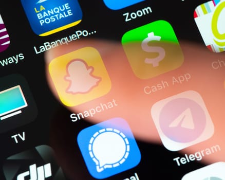BAYONNE, FRANCE - CIRCA JANUARY 2021: Semi transparent finger tap Snapchat app icon on Apple iPhone screen. Snapchat is a multimedia messaging app developed by Snap Inc.