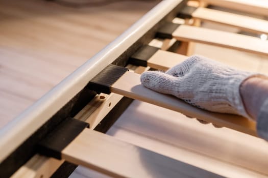 Male worker's hand in glove assembling bed, connecting slats to bed frame.