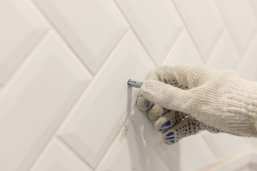 Worker's hand in glove inserts wall pvc dowel in wall cladded with tile ceramic.