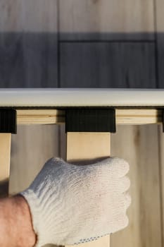 Male worker's hand in glove assembling bed, connecting slats to bed frame.