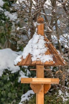 homemade wooden birdhouse or feeder installed on winter garden in snowy day