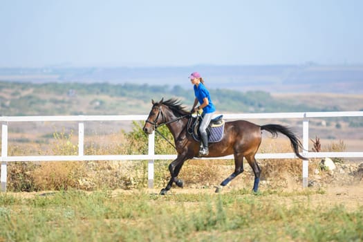 Girl rides a horse along the fence of the corral