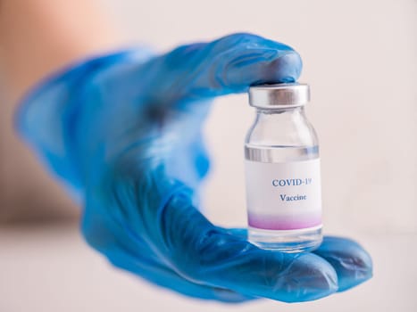 Close-up of a hand in blue medical glove holding a vial with vaccine against COVID-19. Concept of immunization and biotechnological development.