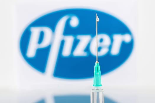 Teo, Spain  December 21 2020: Pfizer Covid-19 vaccine concept Close-up of a syringe and a drop of liquid on it, the Pfizer company logo blurred in the background.