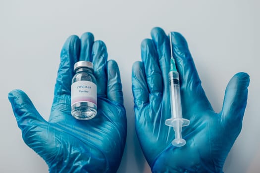 Top view of a hand in blue medical gloves holding a medical syringe and vial with COVID-19 vaccine. Concept of immunization and biotechnological development.