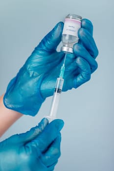 Close-up of a hands in blue protective glove holding a medical syringe and vial. Concept of immunization and biotechnological development.
