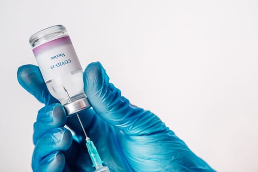 Close-up of a hand in blue medical gloves holding a medical syringe and vial with COVID-19 vaccine. Concept of immunization and biotechnological development.