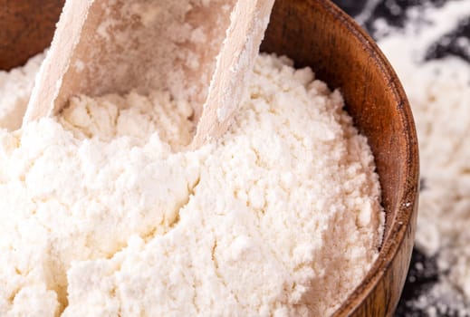 flour in a wooden bowl and shovel on a black background