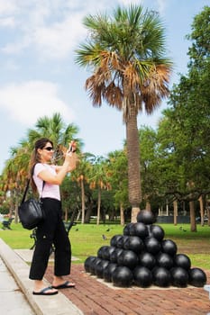 Side profile of a mid adult woman taking a picture in front of a heap of cannon balls