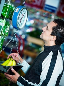 Side profile of a young man weighing a bunch of bananas at a supermarket