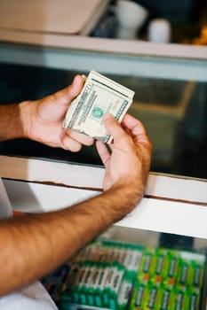 Close-up of a man's hand holding a wad of twenty dollar banknotes