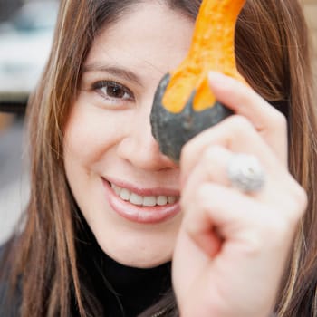 Portrait of a young woman holding a stem of a pumpkin and smiling