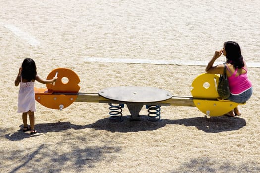High angle view of a girl standing near a seesaw with her mother sitting on it