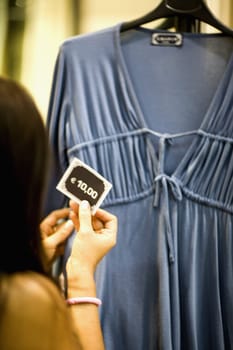 Rear view of a woman checking the price tag of a nightie in a clothing store