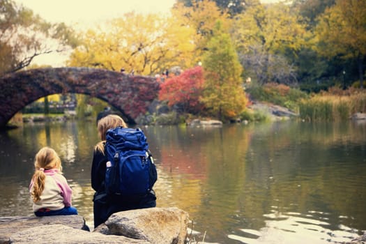 Rear view of a girl and a woman sitting on rocks along a river, New York City, New York State, USA
