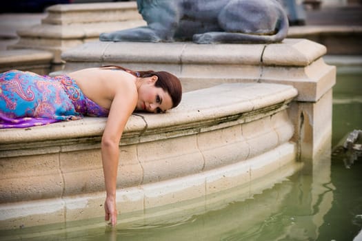 Young woman wearing formal dress dragging hand in fountain water, outdoors