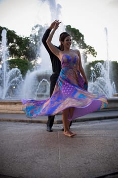 Couple dancing by fountain in plaza, sunset