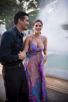 Couple walking by fountain in plaza, sunset